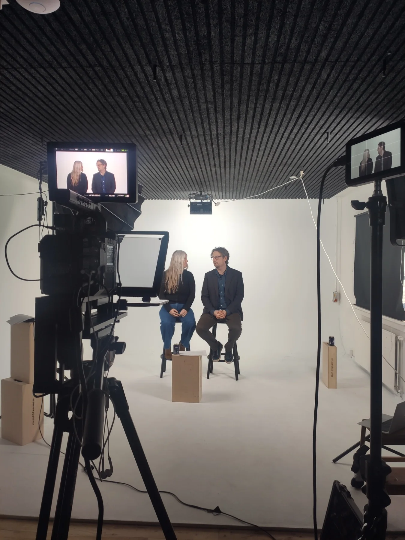 Behind the scenes of a recorded conversation, with two people seated in front of cameras